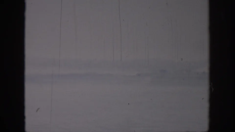 Soft 8mm frame from Oklahoma, 1967, with calm water, a far shoreline, and the view split by a dark window mullion.