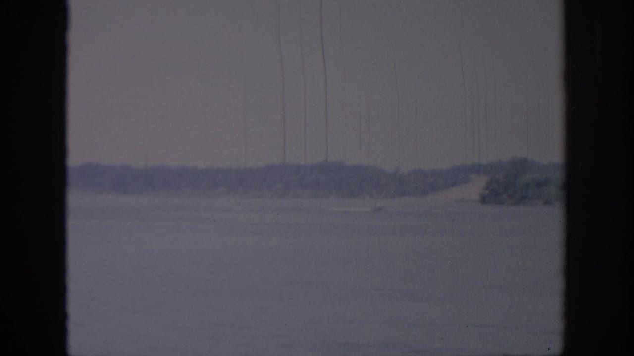 Oklahoma 1967 home-movie frame showing a speedboat near the shoreline, partly framed by dark window bars.