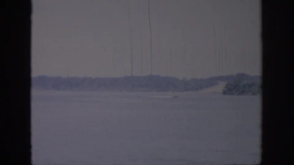 Oklahoma 1967 home-movie frame showing a speedboat near the shoreline, partly framed by dark window bars.