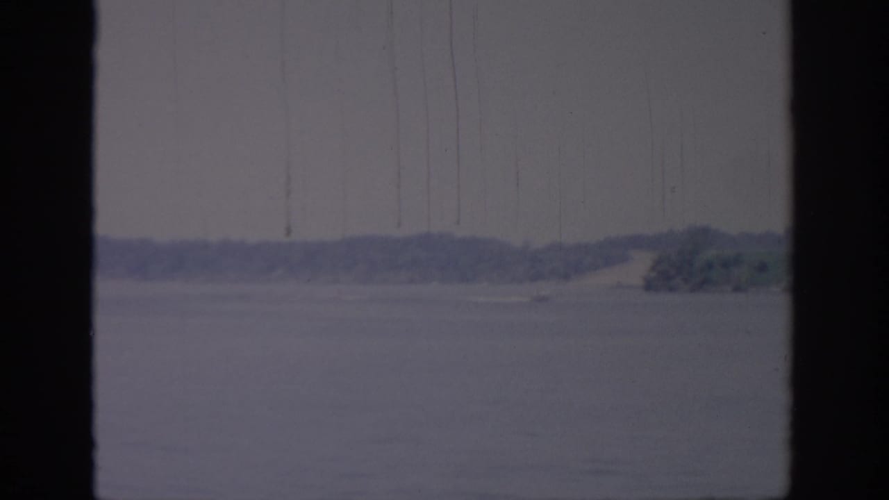 1967 Oklahoma 8mm view of calm lake water and a distant tree-lined shore, framed by dark vertical window edges.