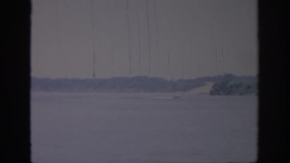 1967 Oklahoma 8mm view of calm lake water and a distant tree-lined shore, framed by dark vertical window edges.