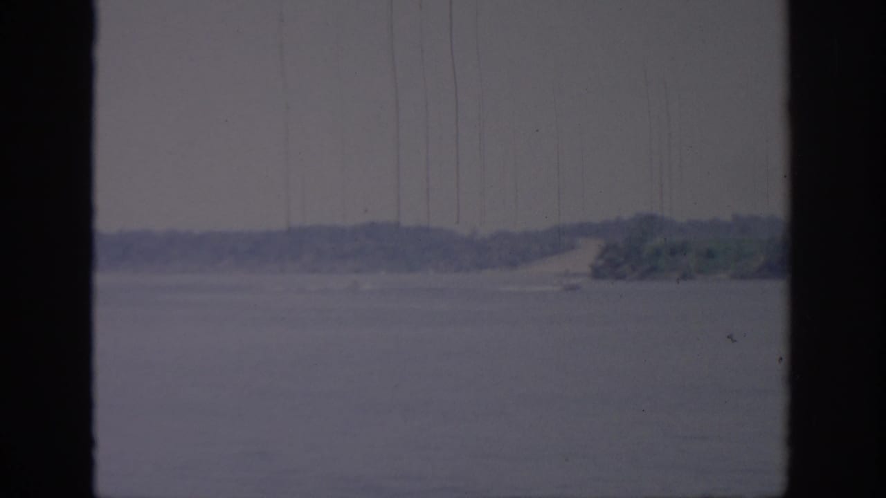 Wide water surface with distant wooded shore and dark vertical framing at both sides.