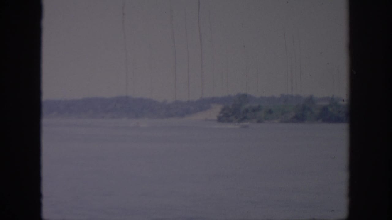Soft 8mm Oklahoma lake view from 1967, showing open water, a distant wooded bank, and visible film scratches.