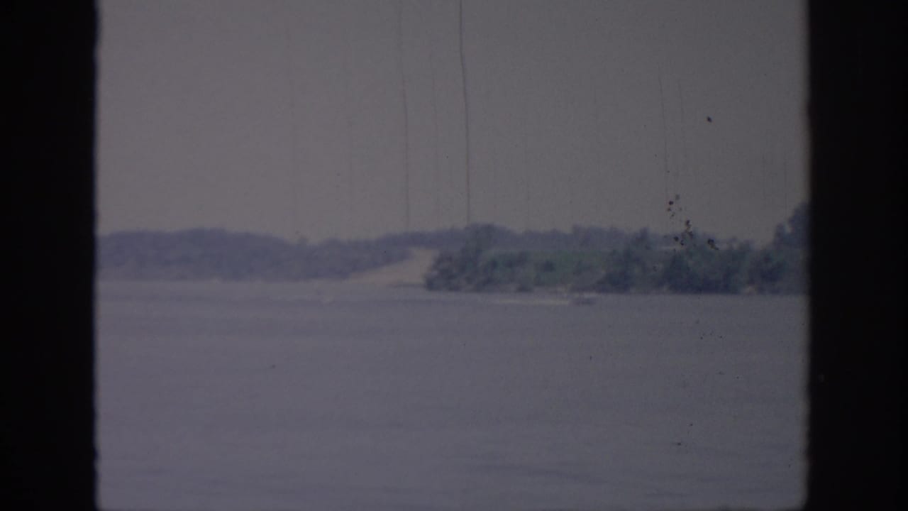 A small boat crosses an Oklahoma lake in 1967, with a faint wake, distant wooded shore, and dark window-like framing.