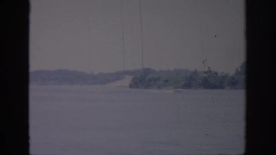 A small boat crosses an Oklahoma lake in 1967, with a faint wake, distant wooded shore, and dark window-like framing.