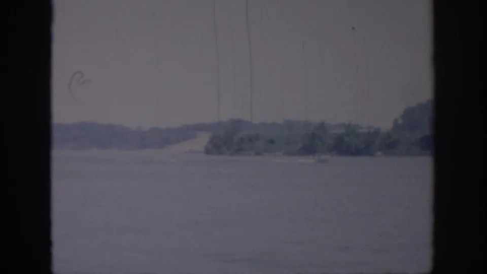 1967 Oklahoma home-movie frame showing a hazy body of water and far shoreline viewed through dark window framing.