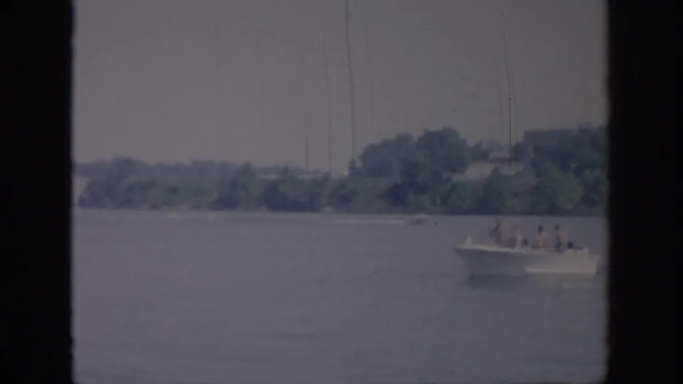 A small white motorboat carrying several distant passengers crosses an Oklahoma body of water in 1967 home-movie footage.