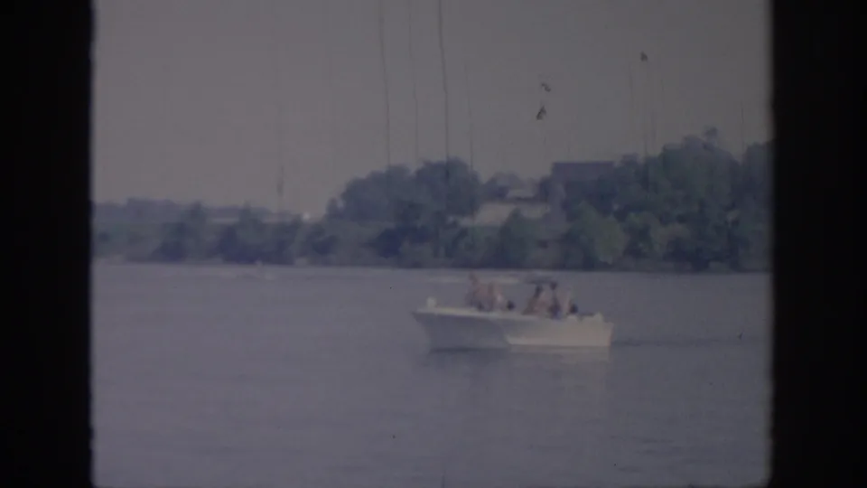 The distant passenger motorboat continues across calm water, with trees and shoreline behind it in 1967 Oklahoma footage.
