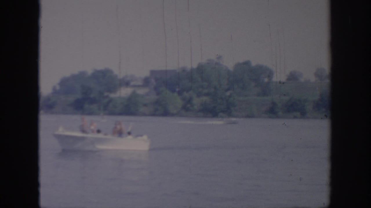 Distant white boat travels across open water with trees and shoreline behind it.