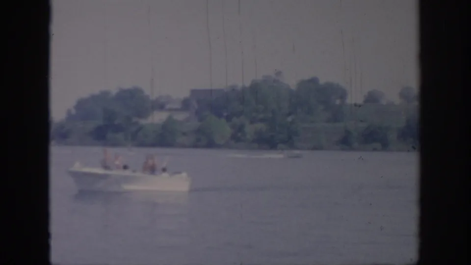 A distant white recreational boat crosses an Oklahoma lake in faded 1967 8mm home-movie footage.
