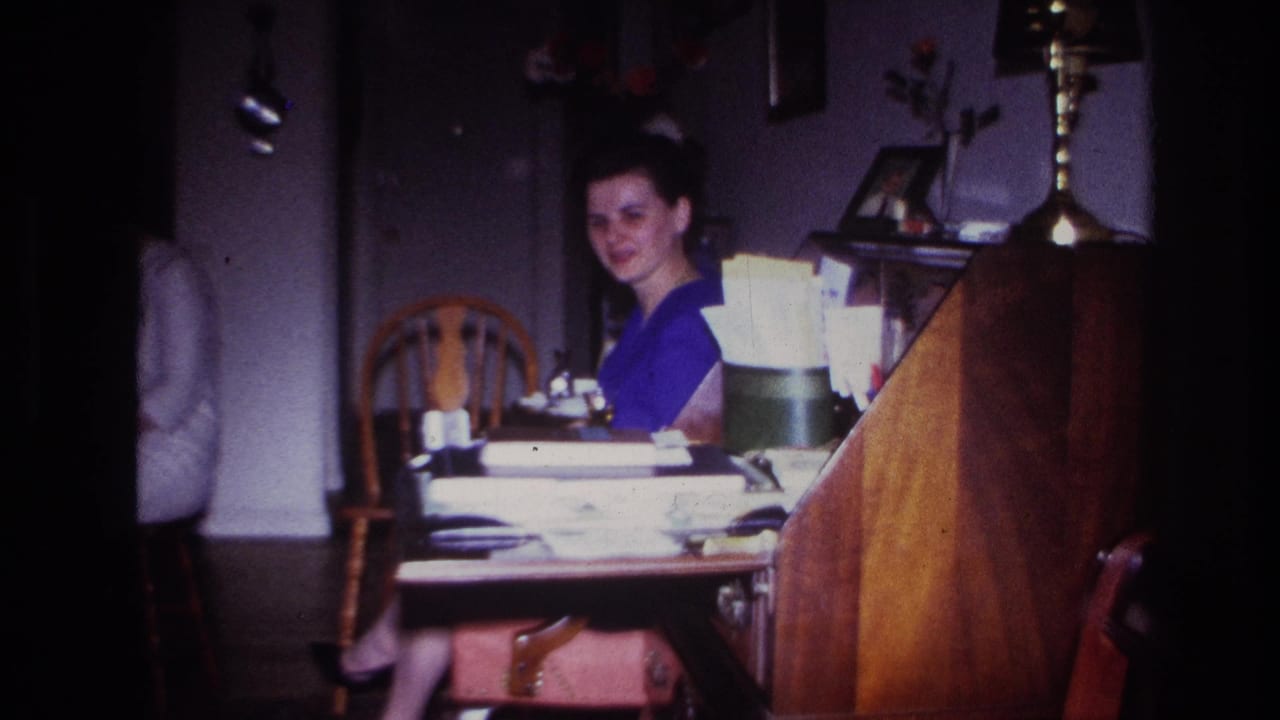Woman in blue turns toward the camera from a cluttered desk.