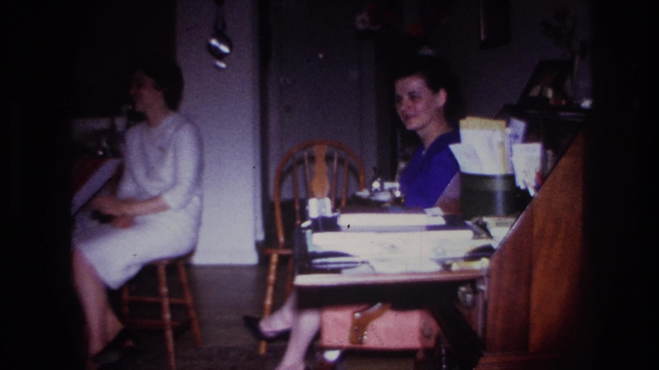 A woman in a light dress sits on a wooden chair while another woman sits at a table.