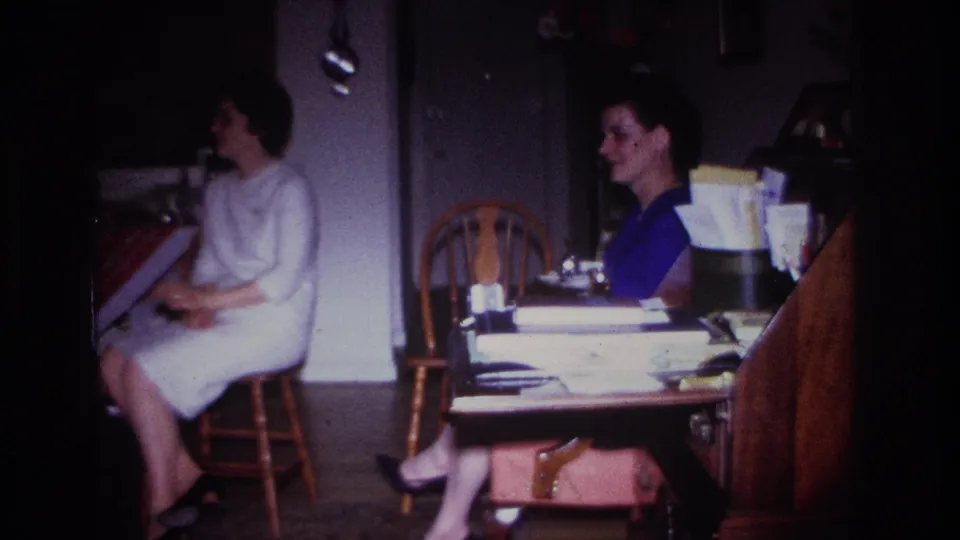 1967 Rockaway Beach home interior with a woman in a light dress seated in profile and another woman partly visible at the table.