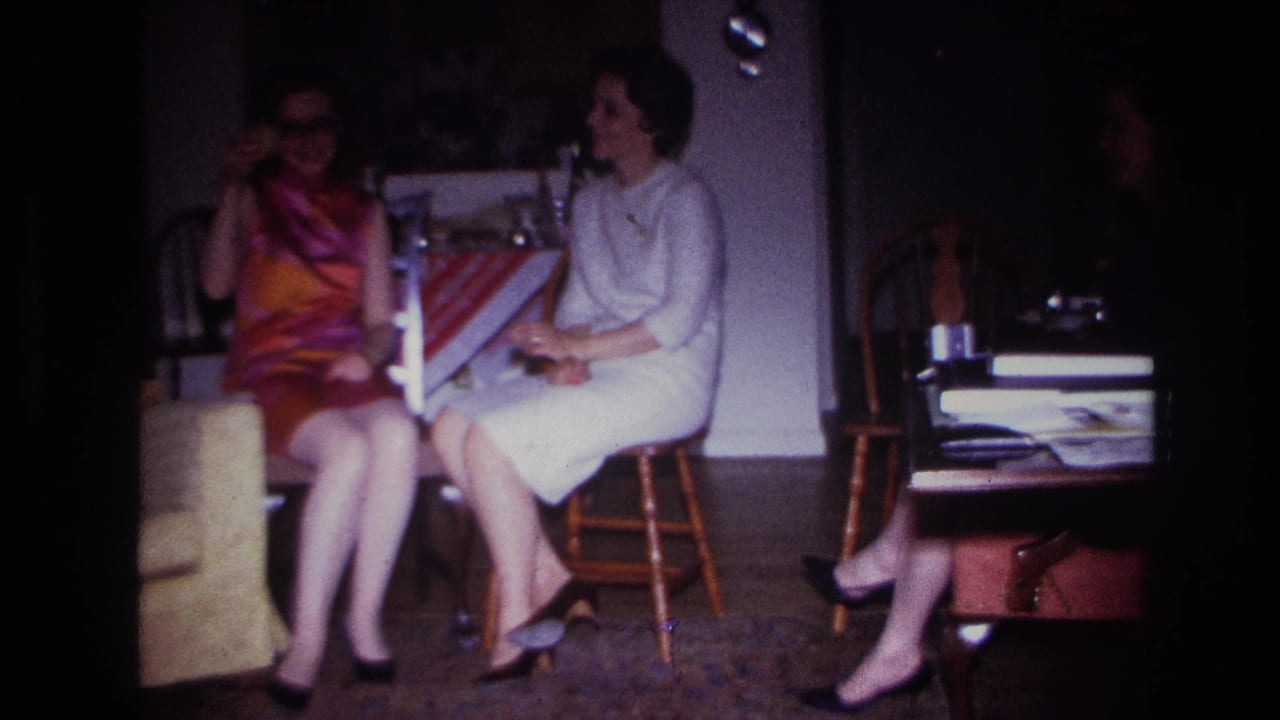 1967 Rockaway Beach home-movie frame showing two adult women seated indoors, smoking and talking in a dim room.