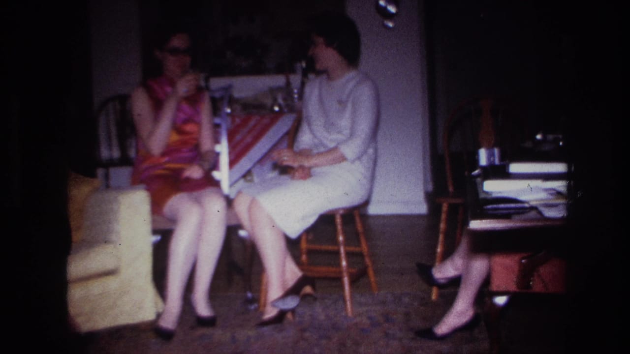 Two seated women face each other while holding cigarettes in a dim home interior.