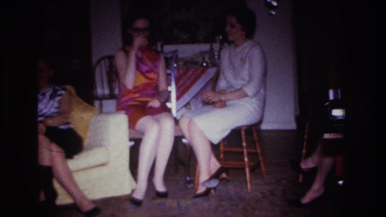 Three adult women seated in a dim living room, with two holding drinks and one in a bright sleeveless dress.