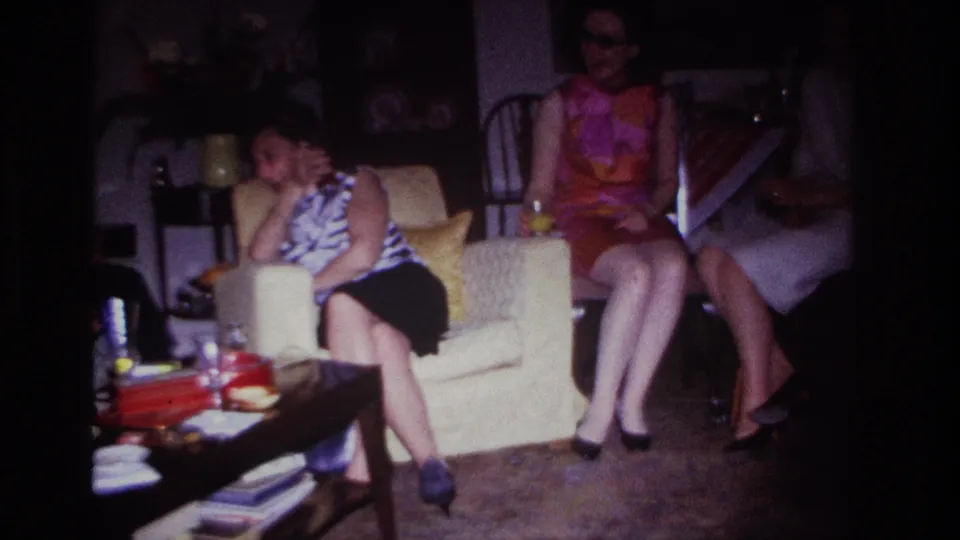 In the 1967 home-movie frame, two women are clearly visible in the living room while a third is partly cropped at the right.