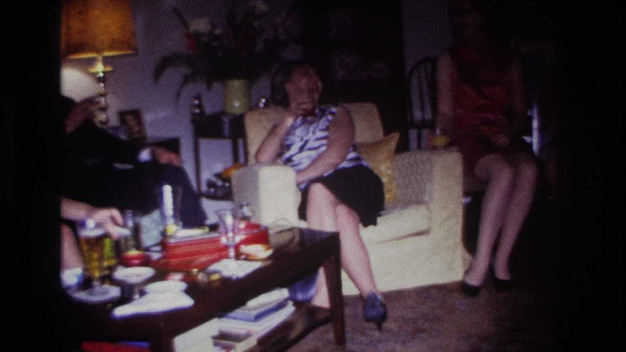 Woman seated on a cream armchair with other adults partly visible beside a coffee table.