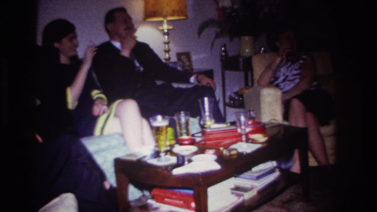 1967 Rockaway Beach home-movie frame showing adults socializing in a dim living room with beer glasses, cigarettes, and books on a coffee table.