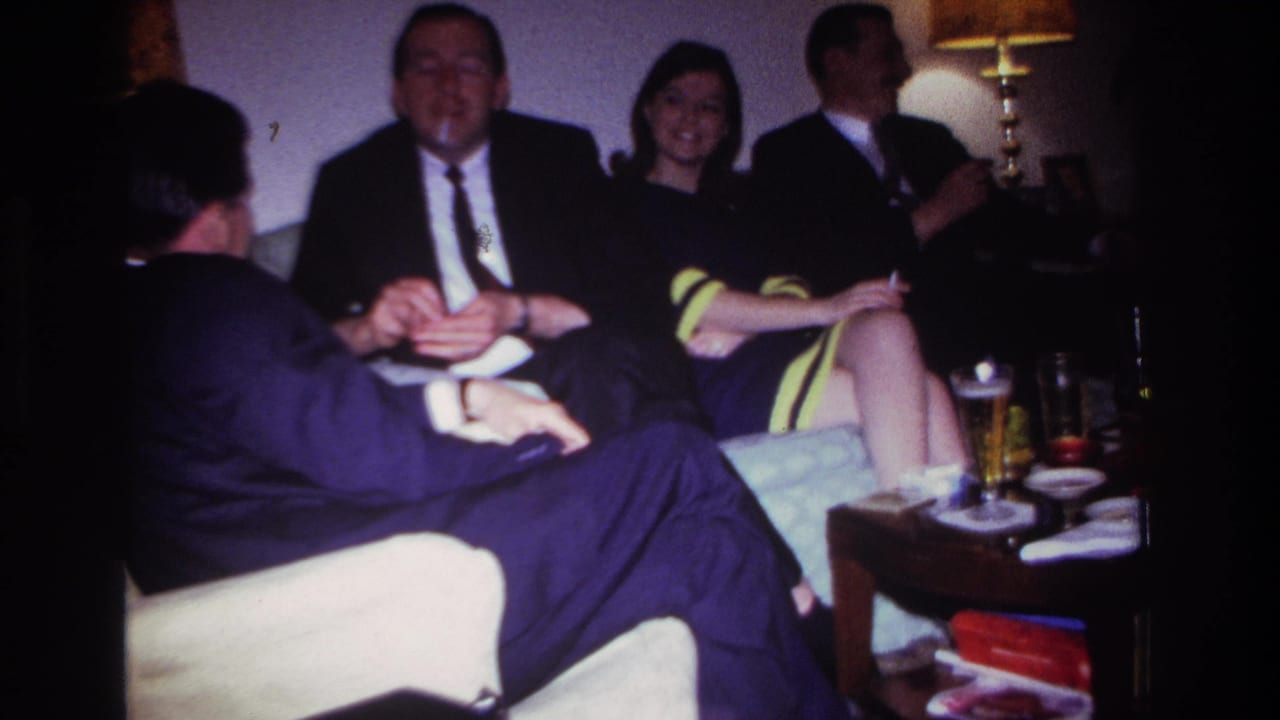 Group of adults smile and talk on living room seating beside a table lamp and drinks.