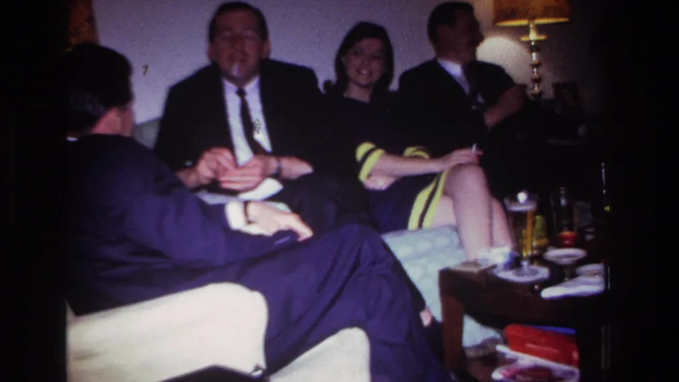 1967 Rockaway Beach frame of adults relaxing on a sofa and chair during an informal evening social gathering.