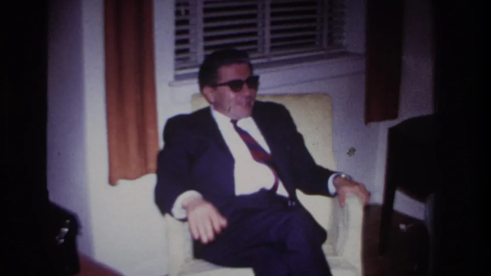 The final frame shows the formally dressed man seated indoors, mouth open as if talking, with the curtained window still visible behind him.