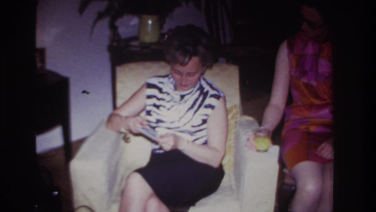 Woman in zebra-print top sits on a white couch looking down at photographs while another woman sits beside her.