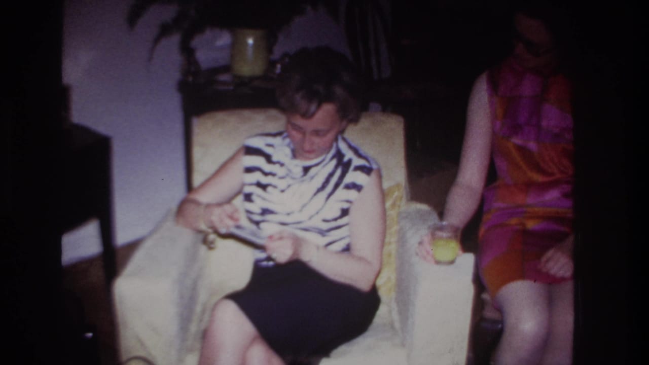 Rockaway Beach 1967 interior frame showing a woman in a zebra-print top reviewing photographs as another woman sits close by with a glass.