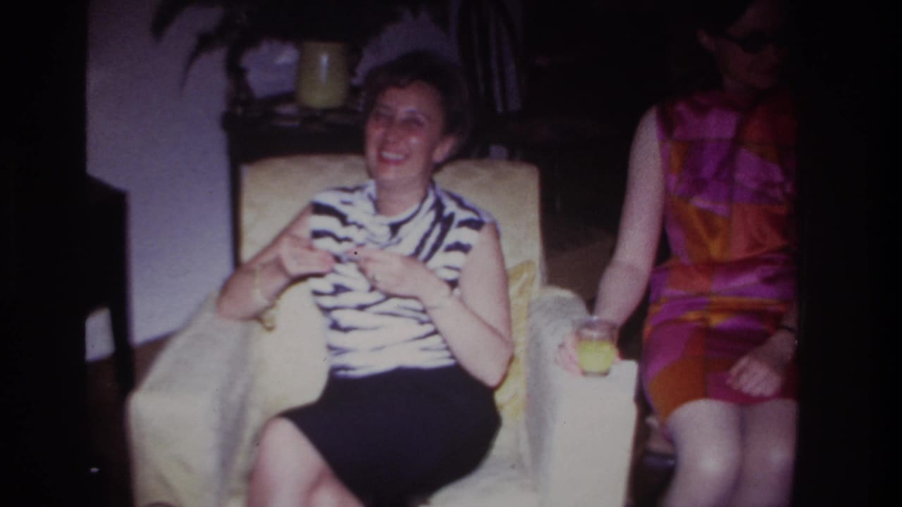 1967 Rockaway Beach frame showing a smiling seated woman in a living room beside a woman in sunglasses and a bright dress.