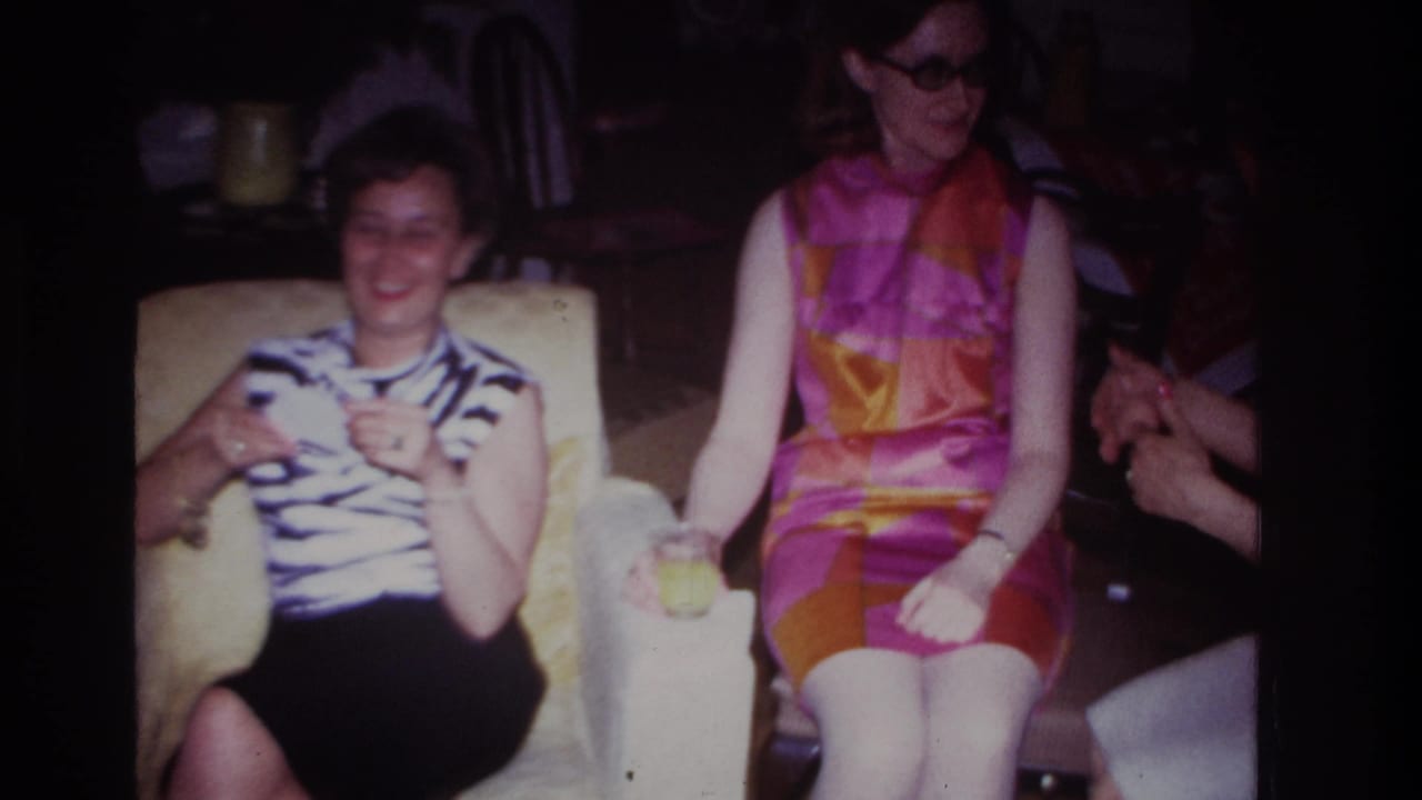 Two adult women seated indoors with drinks, one in a striped top and one in a bright geometric dress.