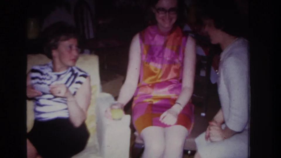 Three adult women socialize in a dim Rockaway Beach interior, with one woman leaning toward the others during conversation.