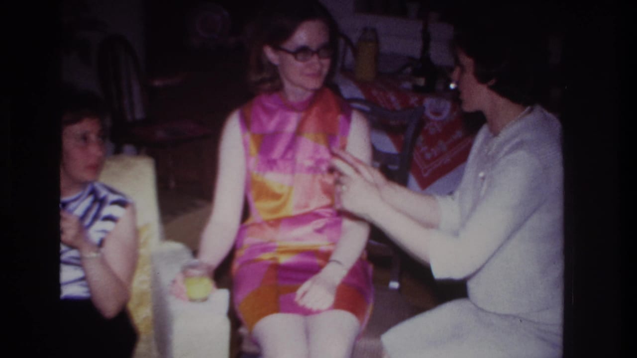 1967 Rockaway Beach interior frame with a woman gesturing toward another woman in a bright dress as a third woman watches.