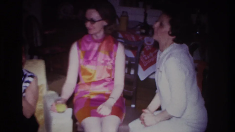 1967 Rockaway Beach living-room frame with the central woman in glasses looking left while another woman sits beside her.