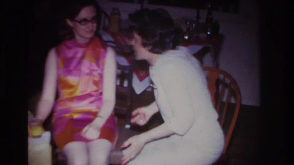 In a 1967 Rockaway Beach home interior, two adult women sit close together during a conversation at a small gathering.