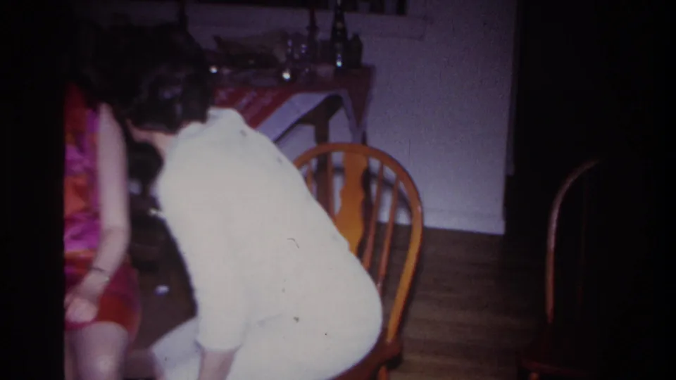 Inside the home interior, the woman in light clothing bends forward near the seated woman as the conversation continues.