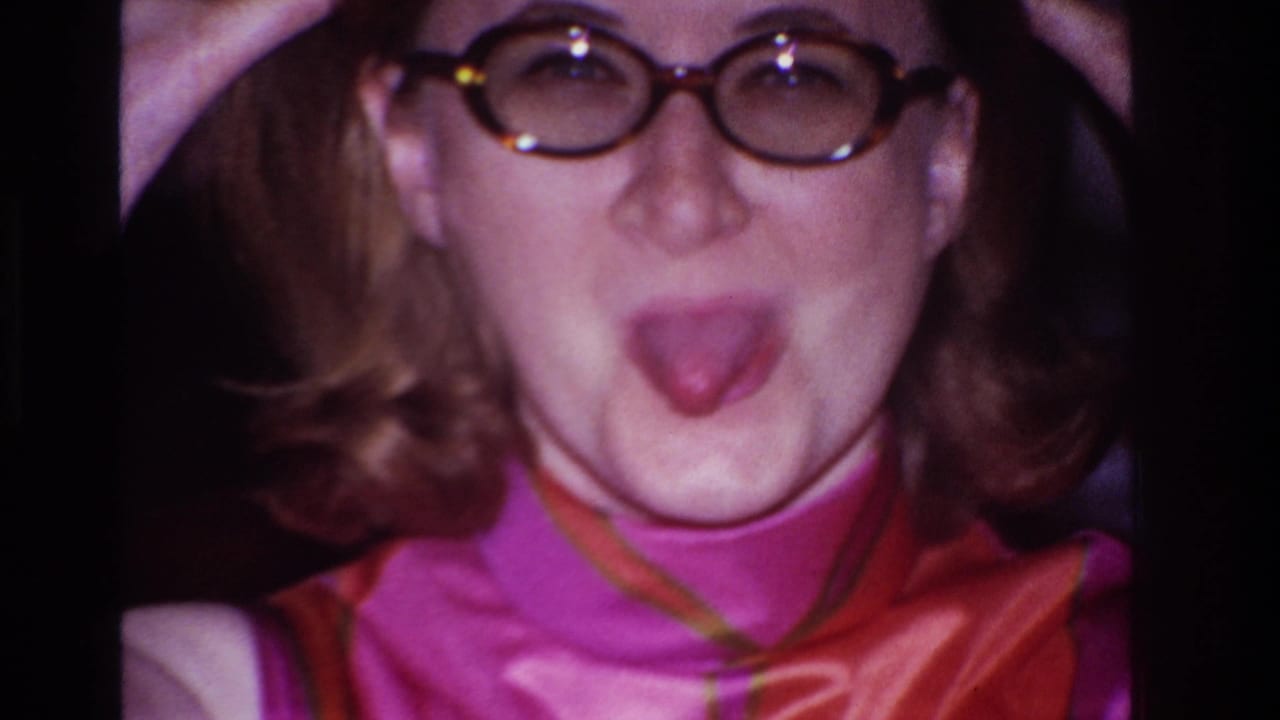 The woman in round glasses sticks out her tongue at the camera, with hands lifted near her head in a playful pose.