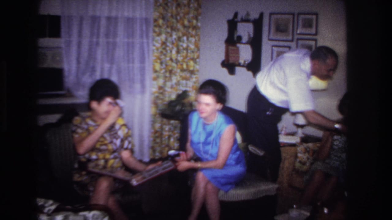 1967 Rockaway Beach living-room frame with two women seated, a photo album open, and a man leaning near a side table.