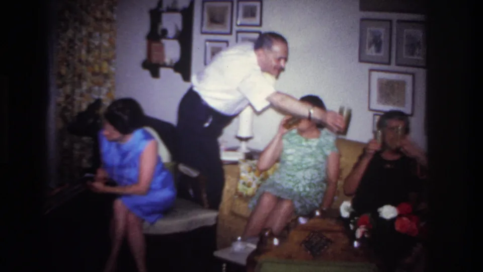 1967 Rockaway Beach interior frame showing a man passing a drink among seated adults in a private living room.