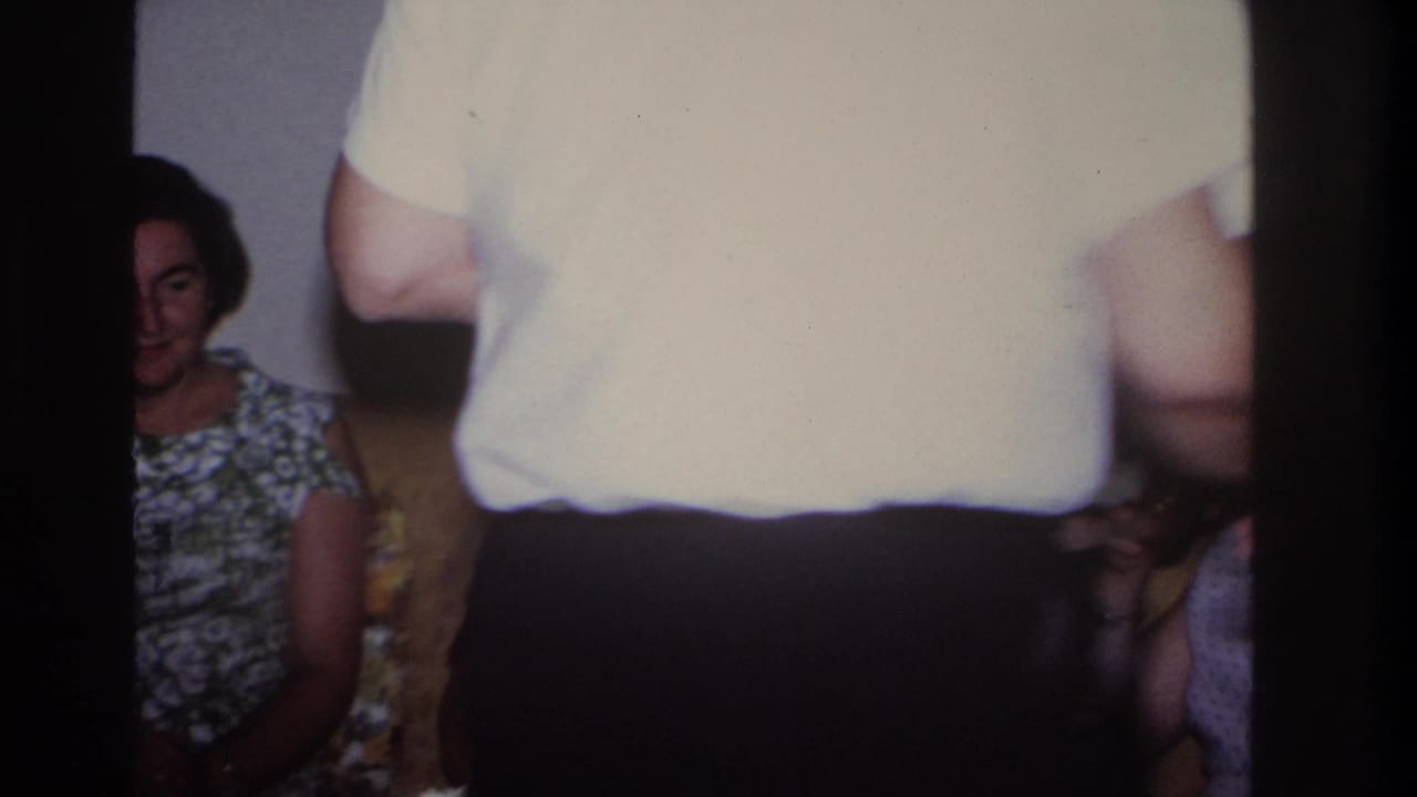 Woman seated on a couch while a man in a light shirt passes in front of the camera.