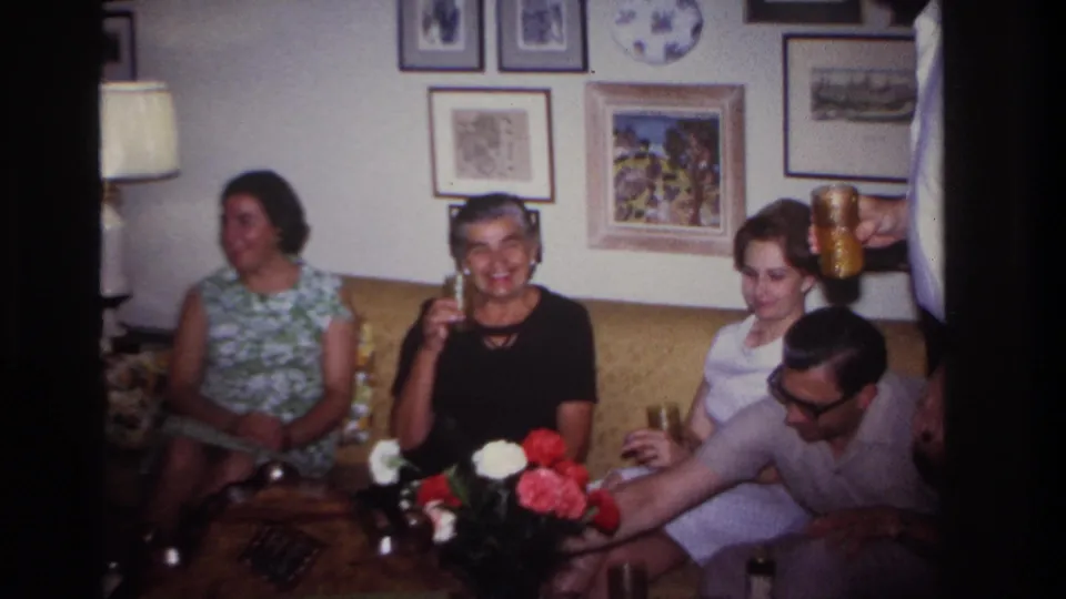 A wider 1967 Rockaway Beach living-room view shows several adults on and near a couch, with drinks, flowers, framed art, and a lamp.