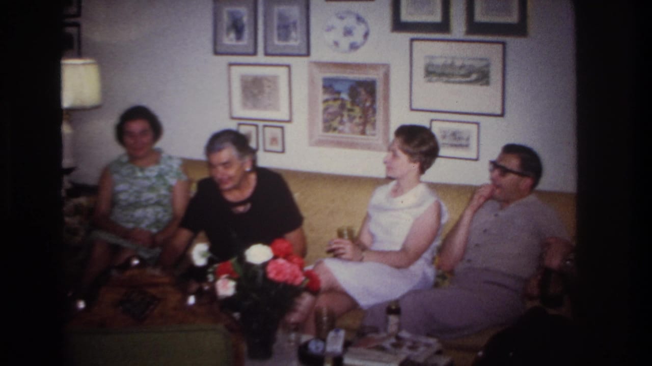 Four adults on a sofa in a living room, holding drinks near framed artwork and flowers.