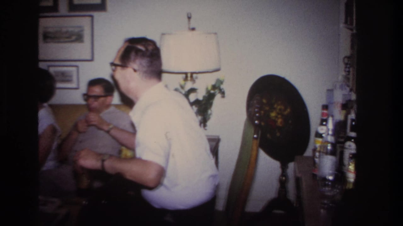 Adults in a living room near a table with bottles and glassware.