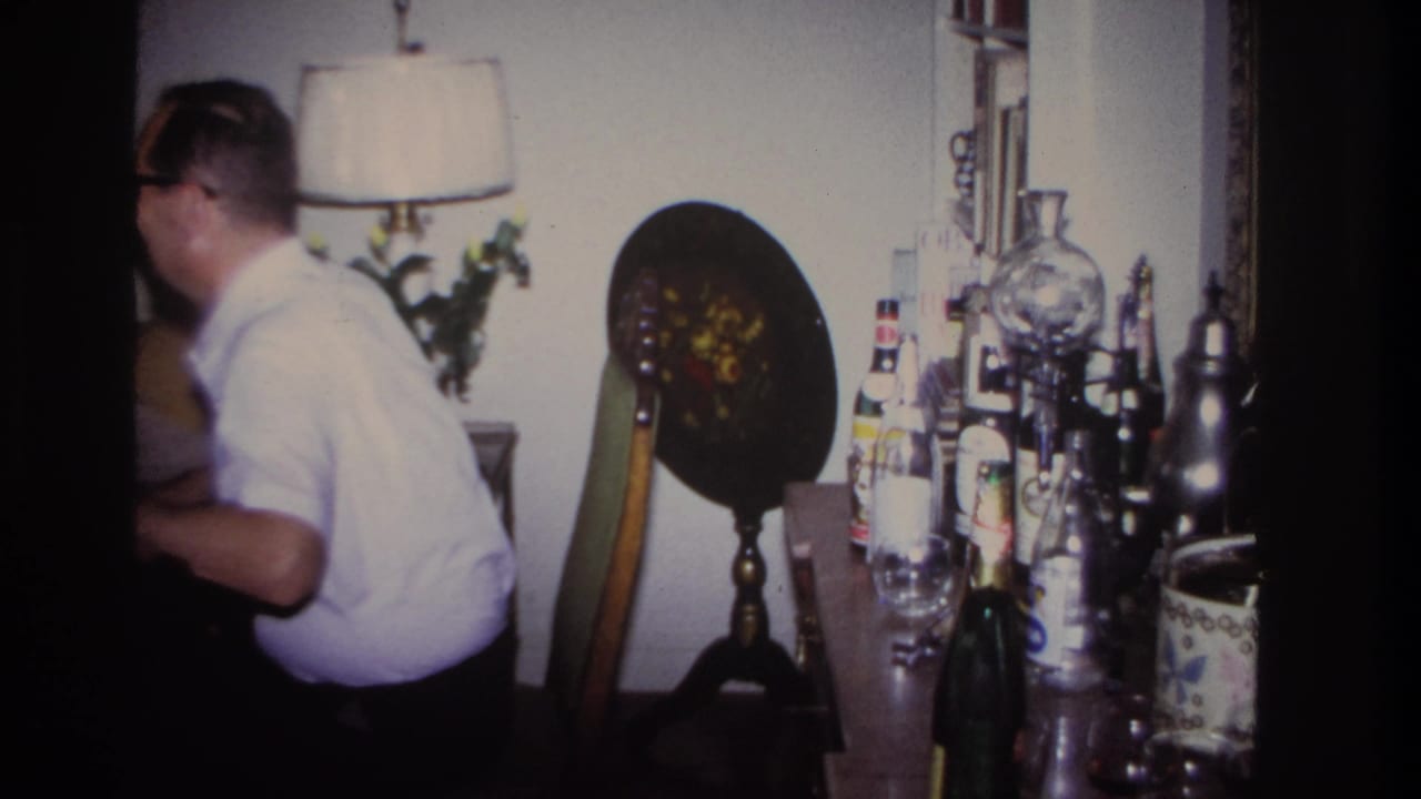 Man in a white short-sleeve shirt stands beside a table of bottles and glassware in a 1967 Rockaway Beach private interior.