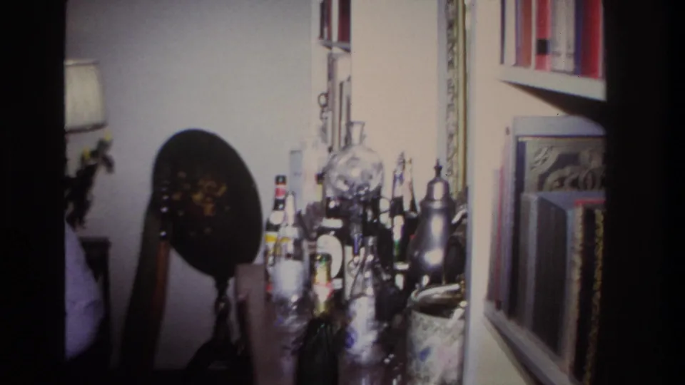 The camera view shifts across a drinks table, decorative globe, lamp, and wall decor inside a 1960s Rockaway Beach living room.