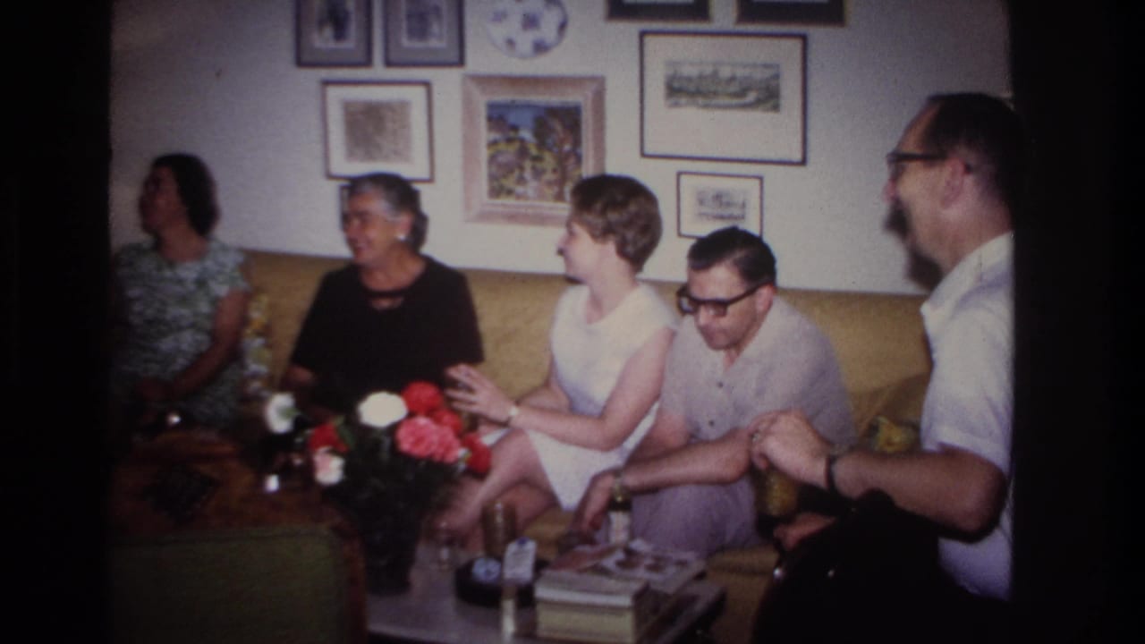Group of adults on a sofa, with a flower arrangement and framed pictures behind them.