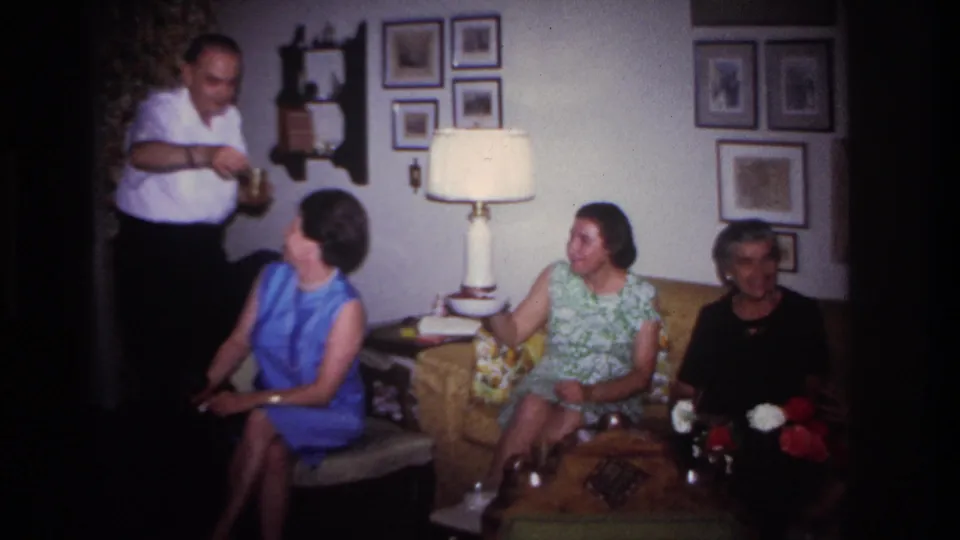 1967 Rockaway Beach living-room scene with a man serving refreshments beside seated women and framed pictures on the wall.