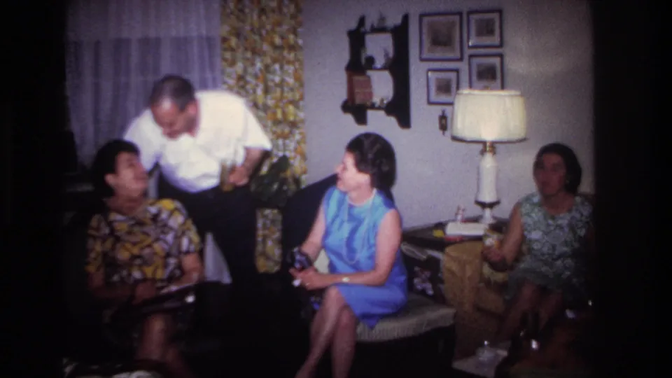 Rockaway Beach 1967 living-room scene with a standing man, three seated women, framed pictures, curtains and a shaded lamp.