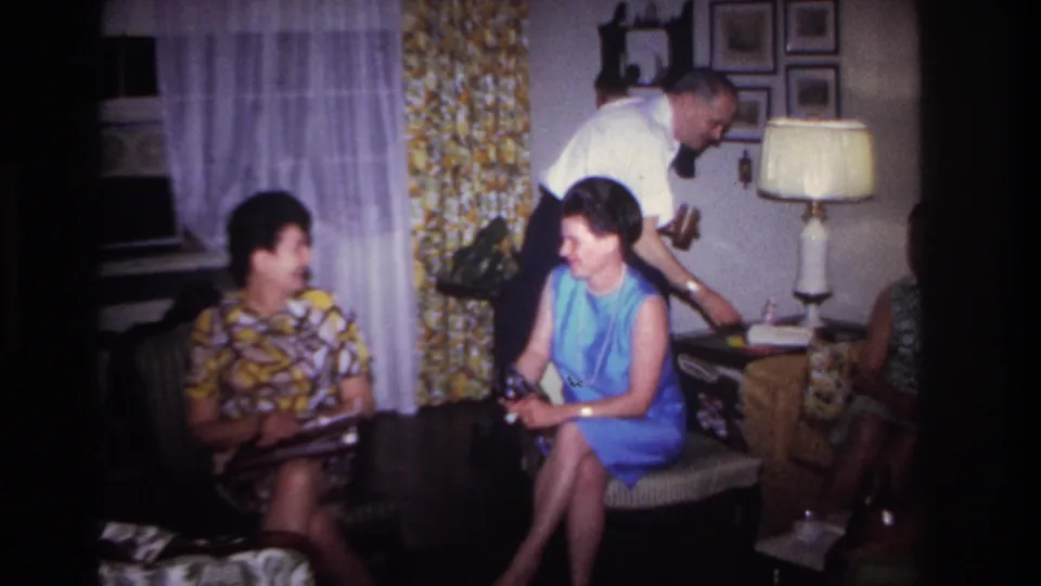 Rockaway Beach 1967 family gathering frame with a man leaning near a seated woman in blue and others seated nearby.
