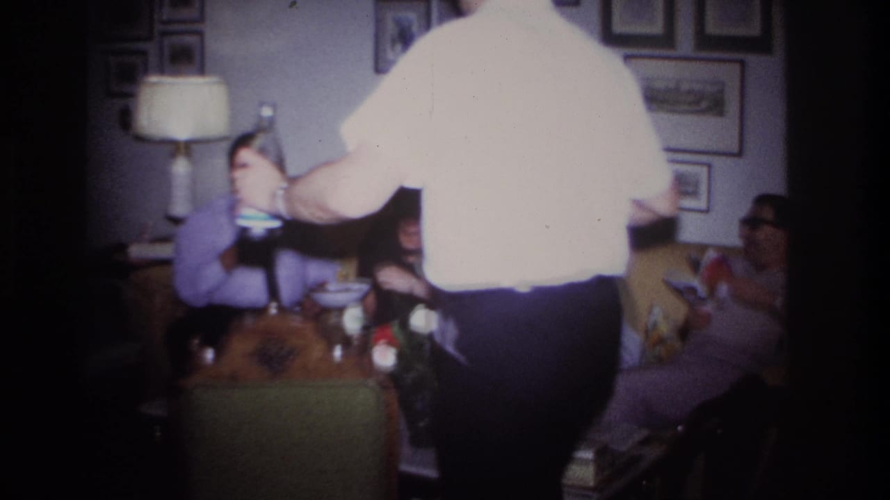 Adults seated in a living room while a man in a white shirt serves drinks.