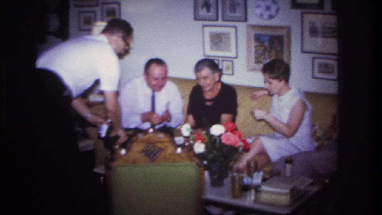 Adults seated on a yellow sofa while a man in a white shirt serves drinks.